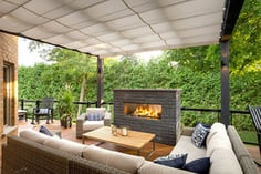 Patio Area with Black Fireplace and patio furniture in front of Green foliage 